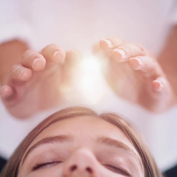 A pair of hands radiate light over the head of a woman